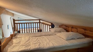 Uma cama de solteiro com peseira e rodapé de madeira num quarto com teto inclinado.