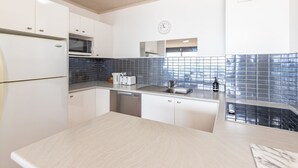 A modern kitchen with white cabinets, a microwave, a toaster, a sink, and a clock on the wall. - Oceanic 3 - On The Beach! (Forster)