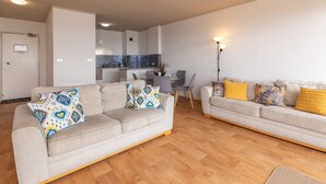 A modern living room with two sofas, a dining table, and a kitchen in the background. - Oceanic 3 - On The Beach! (Forster)
