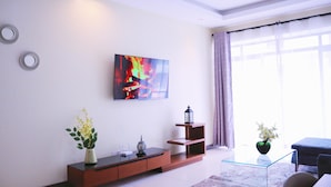 Una sala de estar moderna con una televisión de pantalla plana, una mesa de centro de vidrio, un sofá y un jarrón decorativo con flores.