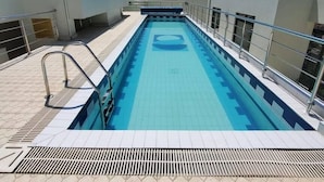 Una piscina en la azotea con una fuente de agua azul cristalina, rodeada por una terraza con azulejos y barandas metálicas.