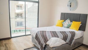Un dormitorio moderno con una cama grande, vistas a través de una puerta corredera y un espejo decorativo en la pared.