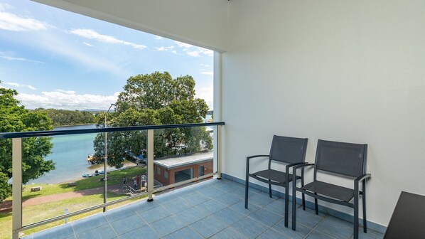 A balcony with a view of a lake and trees, two chairs, and a tiled floor. - The Marina 408 - CBD Location (Forster)