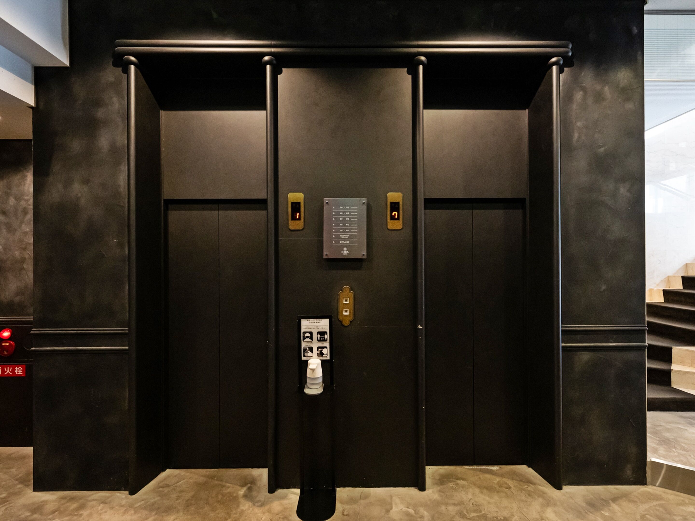 Een moderne lift met keypad en kaartlezer, omringd door donkere wanden en een marmeren vloer.