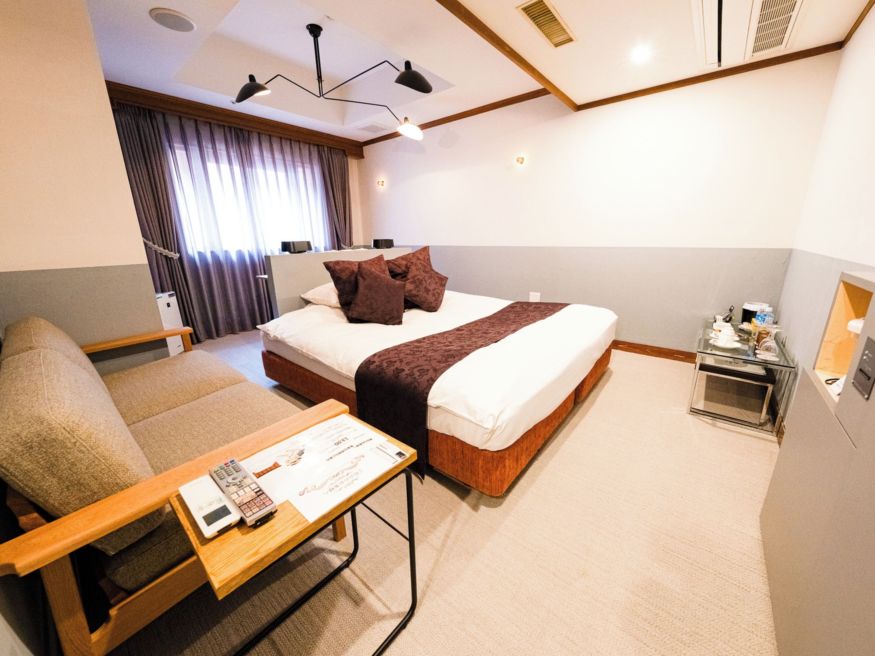 Habitación de hotel con cama, sofá, una mesita con control remoto y una mesita de noche.