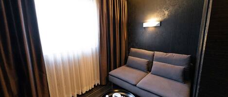 Una sala de estar moderna con un sofá de color oscuro, una mesa redonda de centro y una lámpara fijada a la pared.