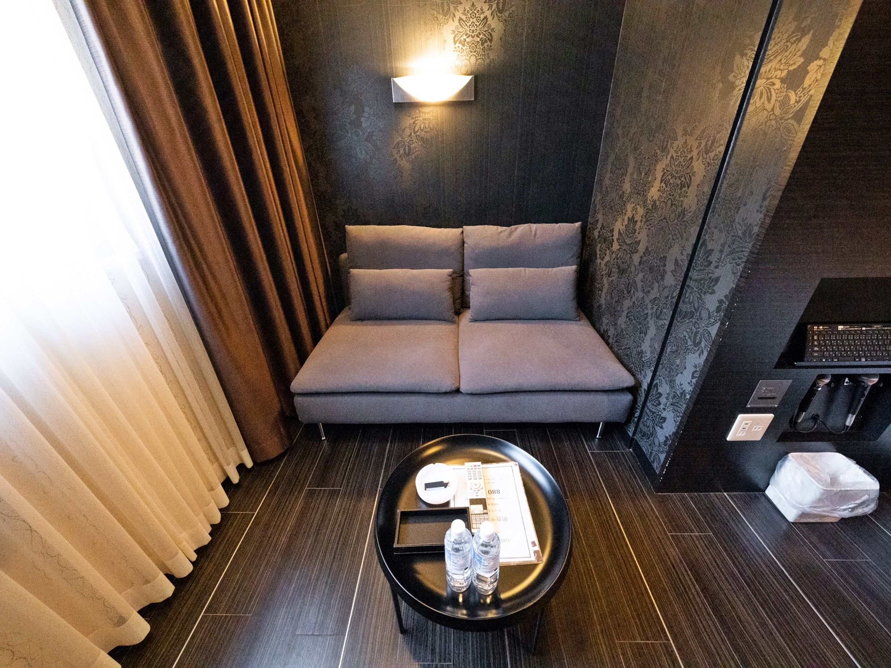 A modern room with a grey sofa, a round coffee table with a tray, bottles, and a remote control.