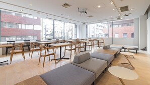 Una sala de conferencias moderna con mesas y sillas de madera, sofás grises y ventanas amplias con vistas a la ciudad.