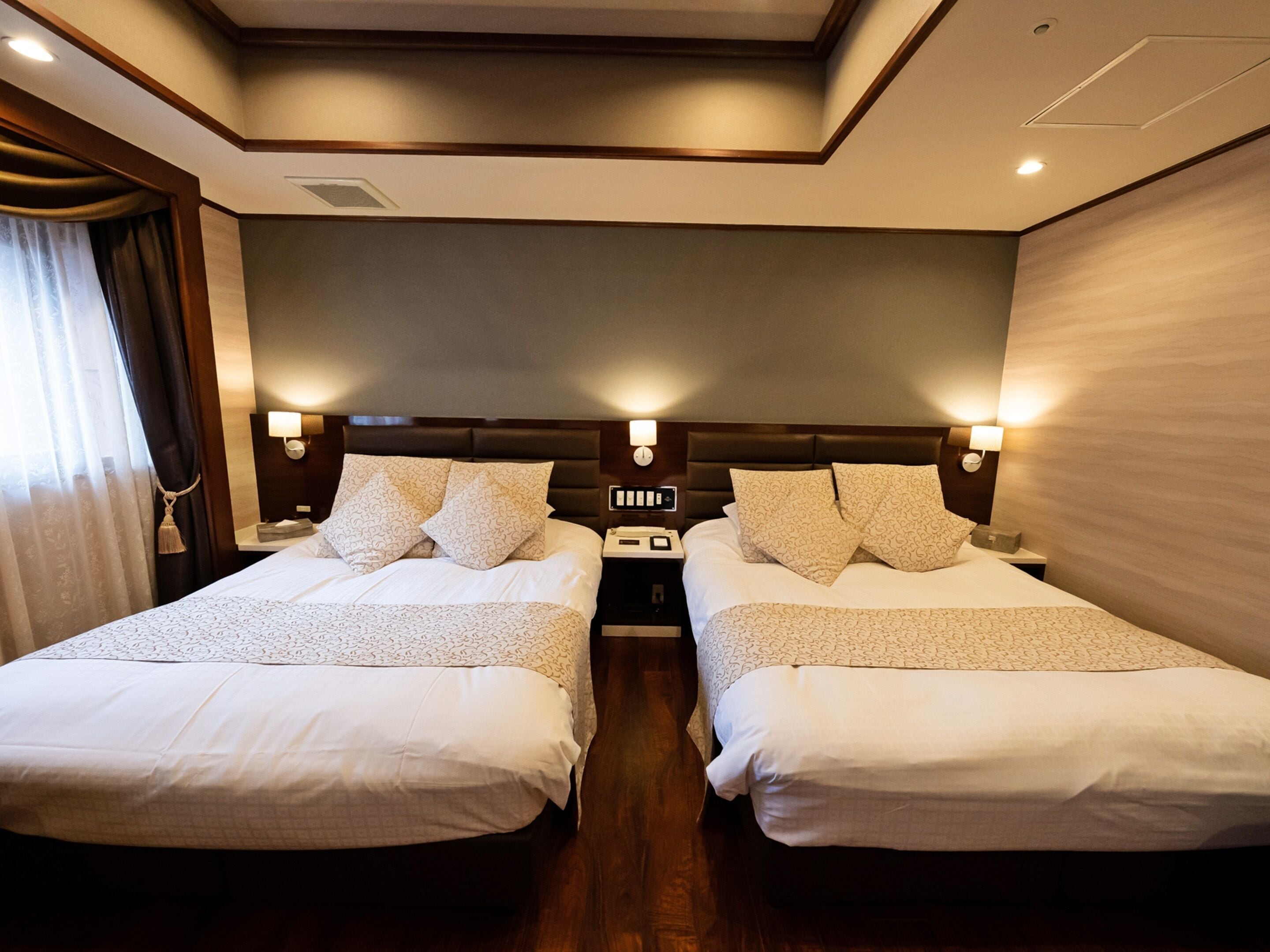 A hotel room with two beds, each with a headboard, bedside tables, and lamps.