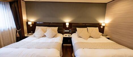 A hotel room with two beds, each with a headboard, bedside tables, and lamps.