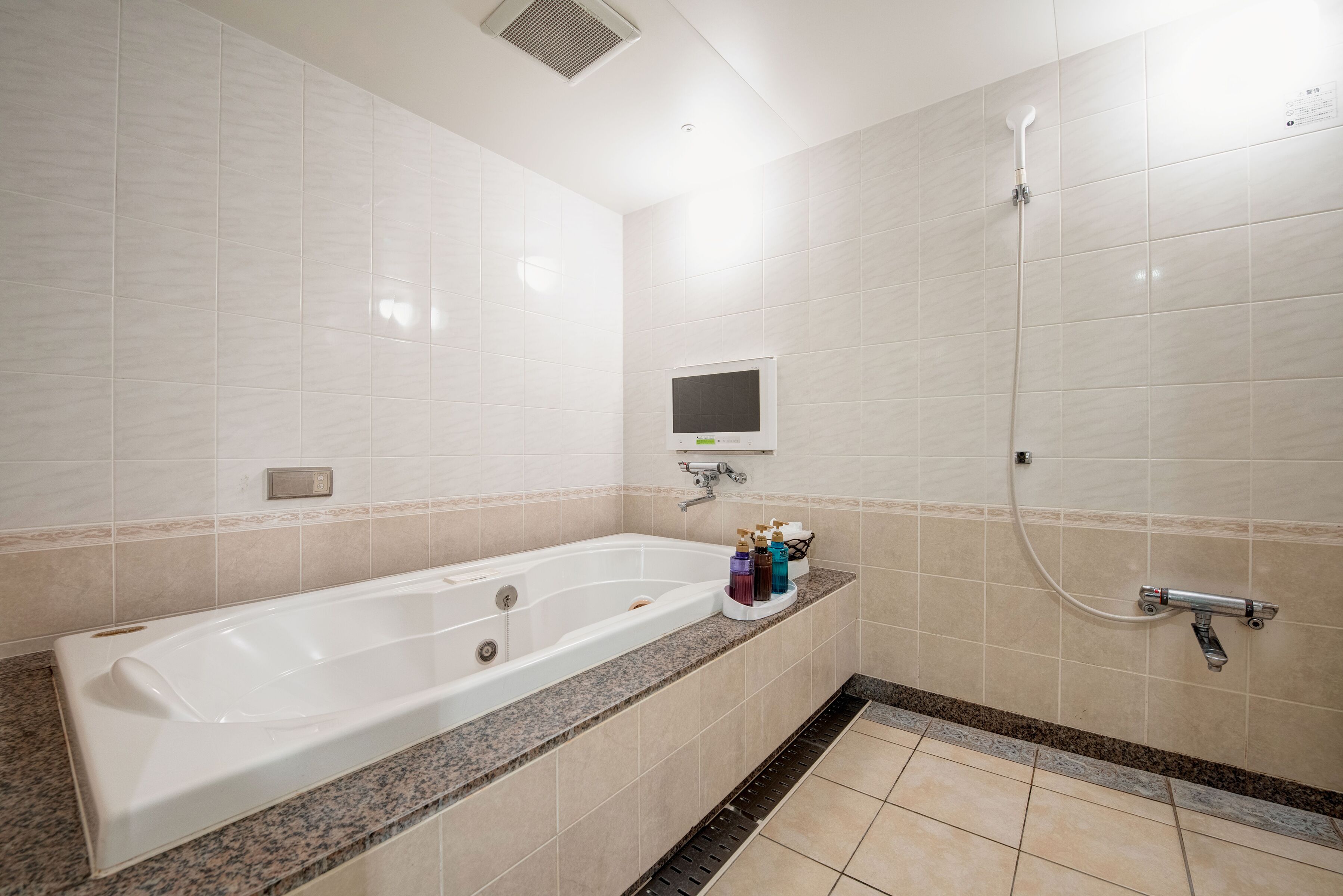 Un baño moderno con una bañera grande, un cabezal de ducha de mano y una pequeña pantalla en la pared.