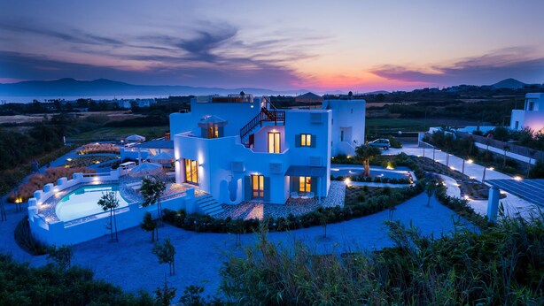 Une maison moderne avec piscine, entourée de jardins aménagés, et offrant une vue sur la mer au coucher du soleil.