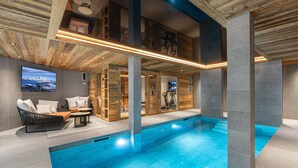 An indoor swimming pool with a wooden ceiling and stone walls, a seating area with a TV, and exercise equipment. - Exclusive Chalet in Courchevel Village (Courchevel 1550)