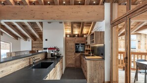 A modern kitchen with wooden beams, a black countertop, and a stainless steel refrigerator. - Exclusive Chalet in Courchevel Village (Courchevel 1550)