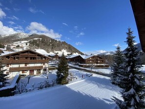 Ein schneebedecktes Bergresort mit Holzhäusern, einer Skipiste und blauem Himmel.