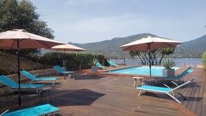 A wooden deck with a pool, blue lounge chairs, and umbrellas. - Mini-villa T2 - Résidence Terra Théa**** (Propriano)