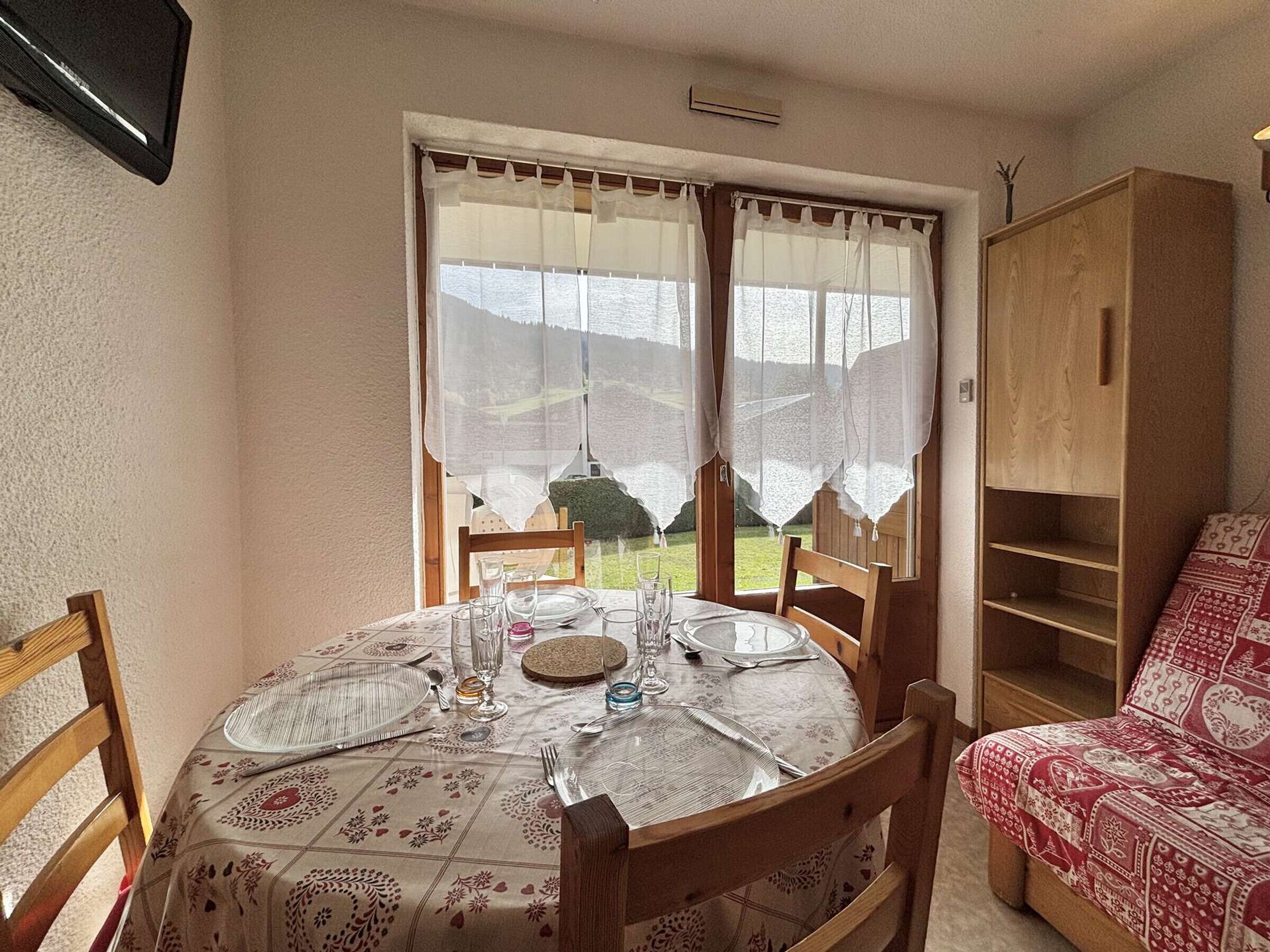 A dining area with a table set for four, a wooden chair, a cabinet, and a patterned sofa.