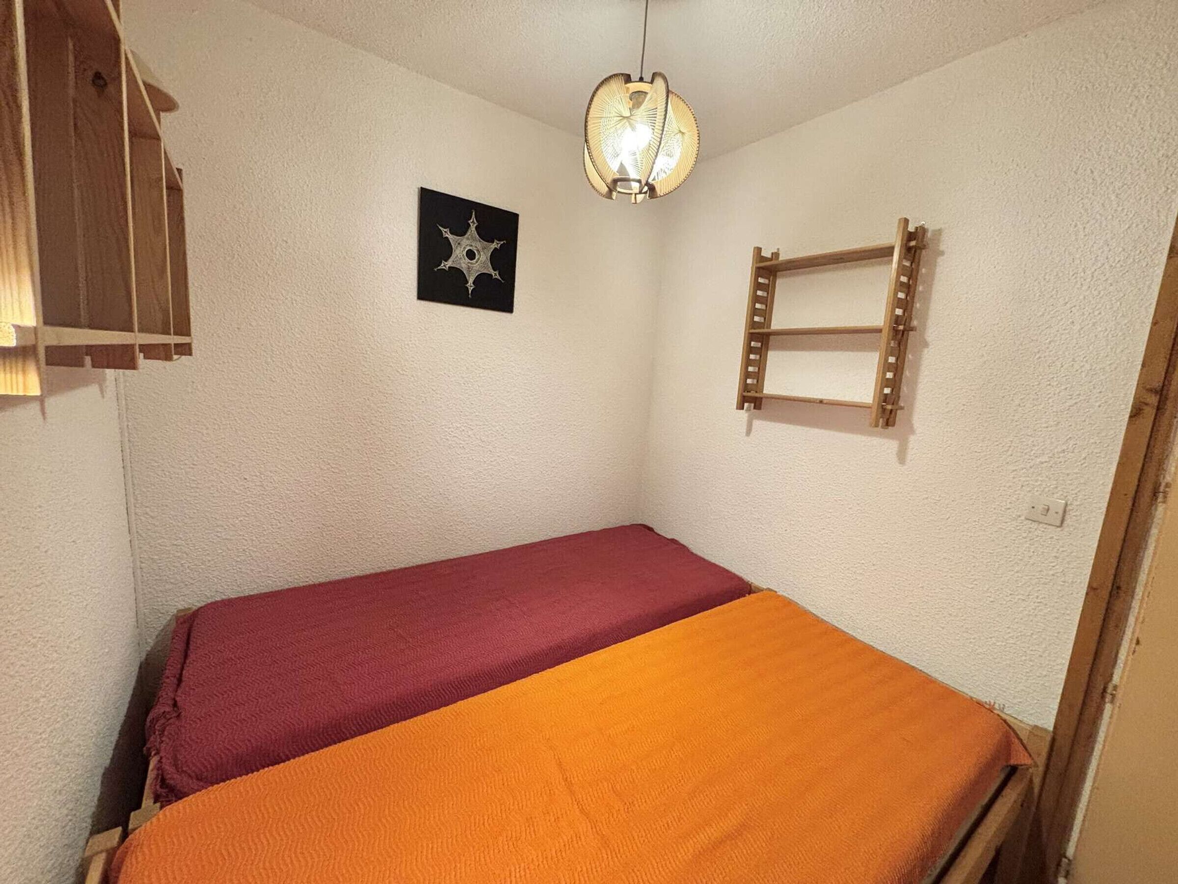 Una habitación pequeña con una cama individual, una estantería de madera con escalera, una lámpara de pared y un adorno con forma de estrella.