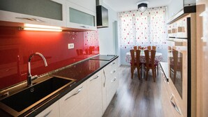 A modern kitchen with a red backsplash, stainless steel appliances, and a dining area with a table and chairs. - Apartment Nostalgija Split (Split)