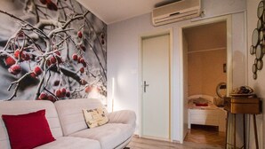 A modern living room with a beige sofa, a red pillow, a wall-mounted air conditioner, and a wooden floor. - Apartment Nostalgija Split (Split)