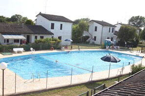 A swimming pool with a tiled deck, surrounded by white buildings with dark roofs.