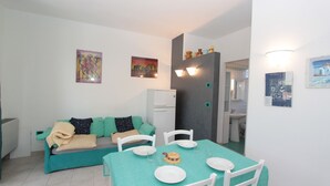 A dining area with a table set for four, a sofa, and a refrigerator in the background.