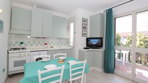 A kitchen with white cabinets, a dining table with chairs, a television, and a view of the outdoors through a sliding glass door.