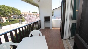 A balcony with a white table and chairs, a TV mounted on the wall, and a view of the street and houses.