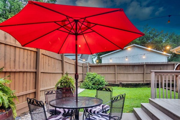 A patio with a red umbrella, a round metal table, and four chairs.