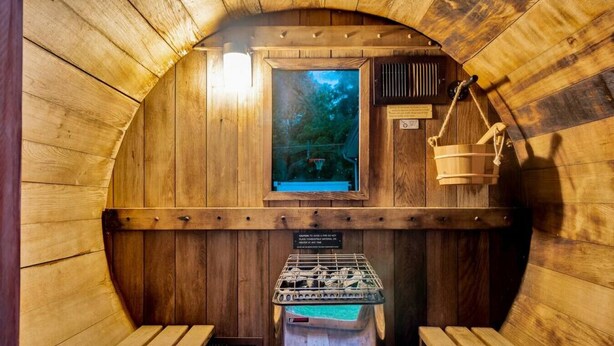Een houten sauna met banken, een raam met uitzicht en een hangmand.