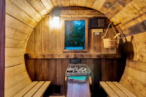 A wooden sauna with benches, a window with a view, and a hanging basket.