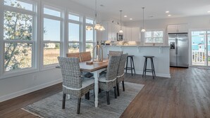 Una cocina moderna con armarios blancos, un refrigerador de acero inoxidable y un comedor con sillas de mimbre y una mesa de madera.