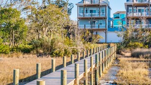 Un paseo marítimo de madera que conduce a propiedades frente a la playa, con varios pisos y balcones.