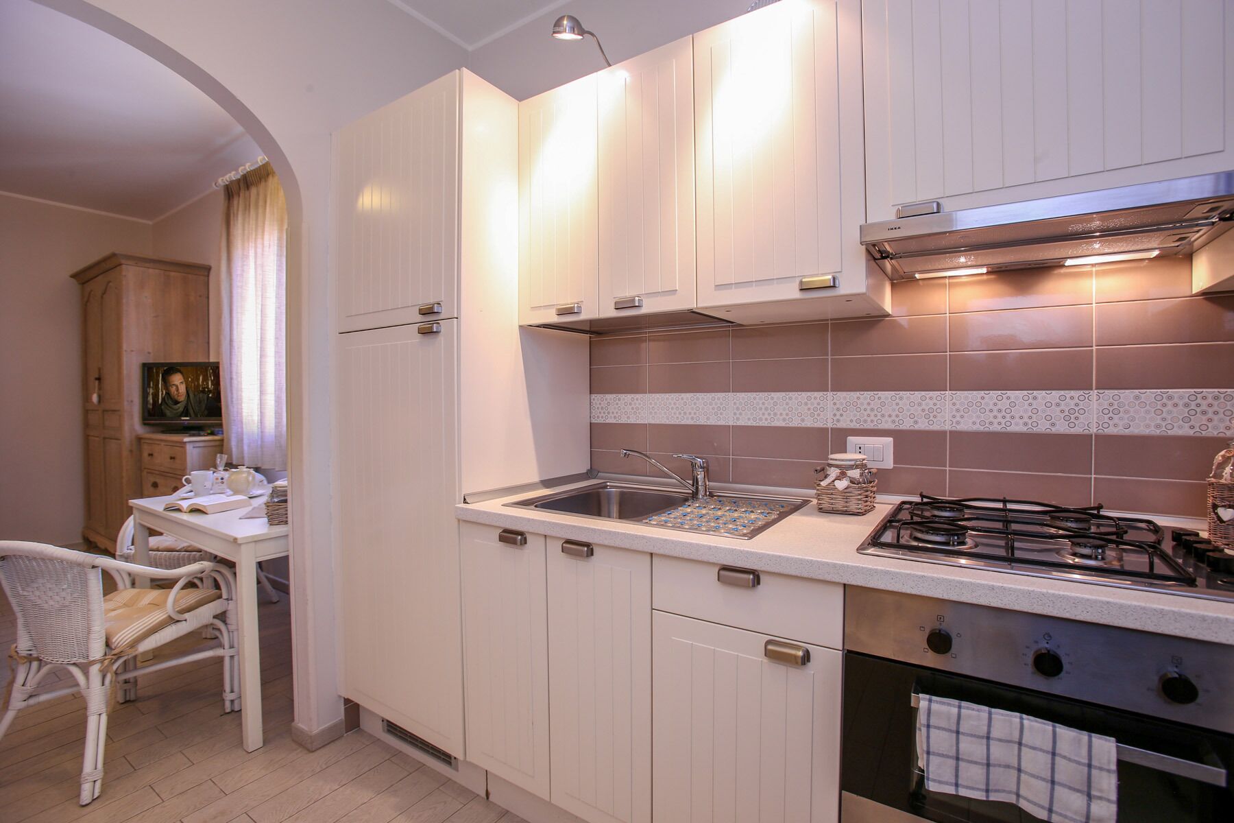 Una cuina moderna amb armaris blancs, una cuina de gas i un forn integrat.