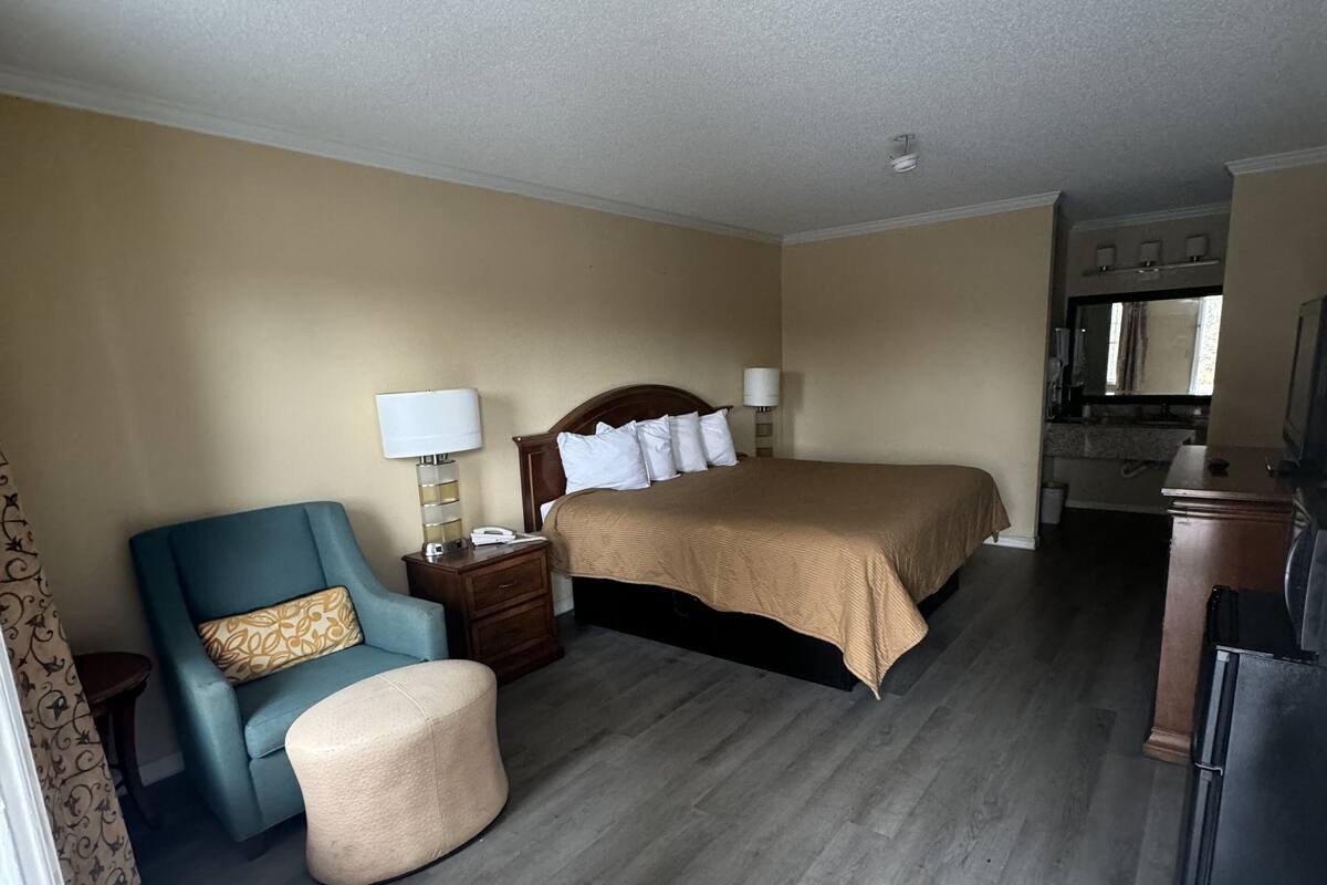 Una habitación de hotel con cama, una silla, un escritorio y una kitchenette.