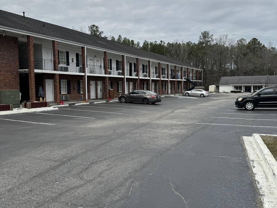 A row of motel-style buildings with a parking lot in front.