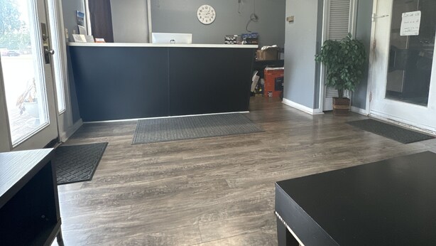 A room with a wooden floor, a black table, a reception desk, a clock, and a door with a sign.
