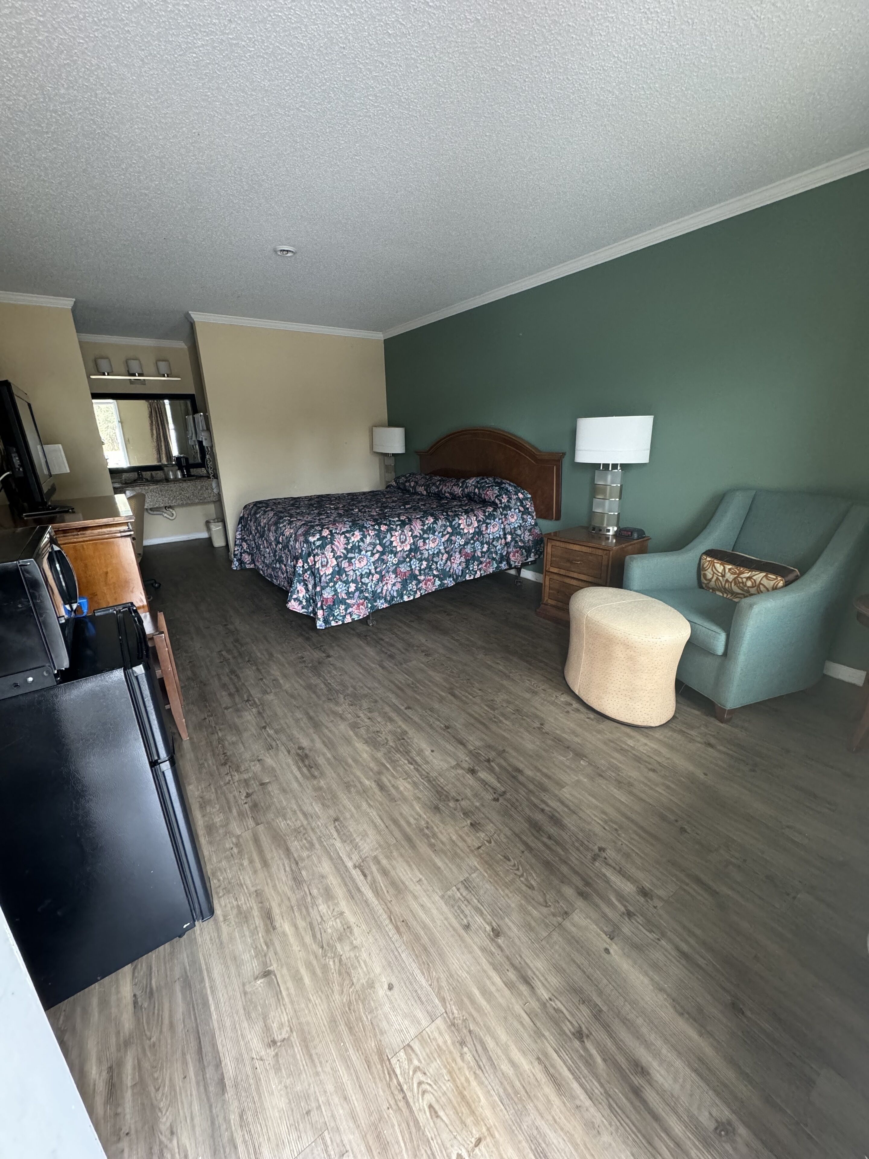 Quarto de hotel com cama, escrivaninha, cadeira, luminária e um pequeno banquinho.