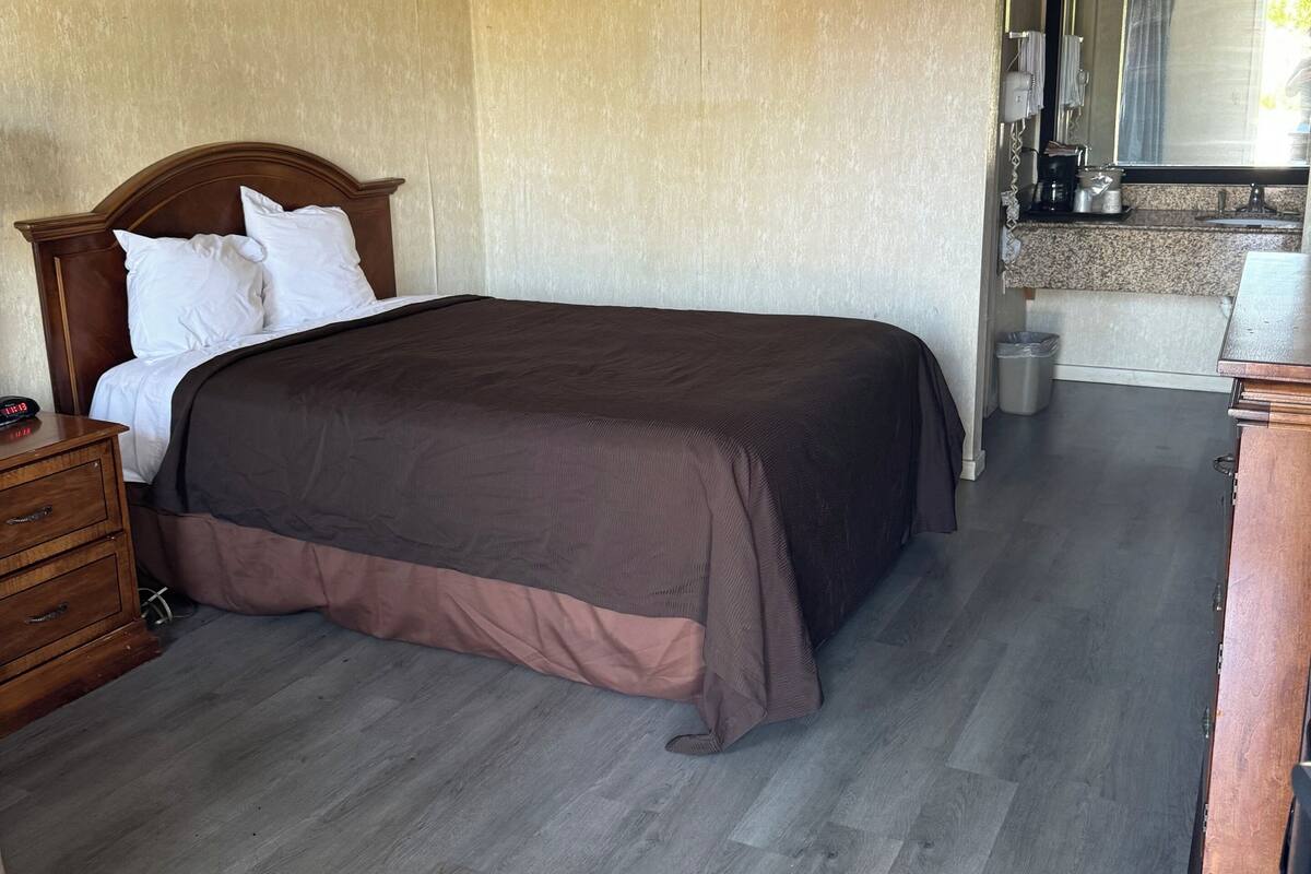 Un dormitorio con una cama grande, cabecera de madera y un aparador. Hay un escritorio pequeño y un espejo en la esquina.