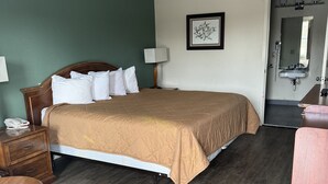 A hotel room with a bed, bedside table, lamp, and a bathroom visible through an open door.
