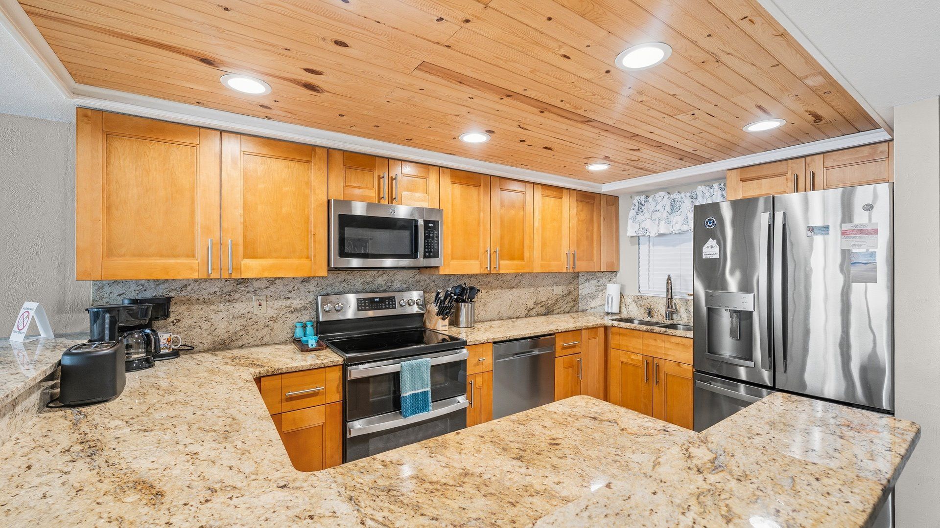 A kitchen with wooden cabinets, granite countertops, stainless steel appliances, and a wooden ceiling.