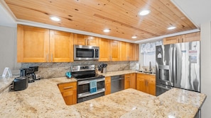 A kitchen with wooden cabinets, granite countertops, stainless steel appliances, and a wooden ceiling.