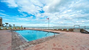 Una piscina con vista al océano, rodeada de sillones de descanso y una valla.