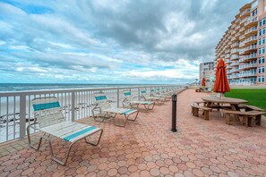 Eine Terrasse direkt am Strand mit Liegestühlen und Tischen, mit Blick auf das Meer.