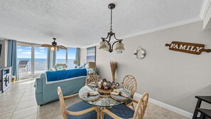A spacious living area with a balcony overlooking the ocean, a dining table with chairs, and a 'FAMILY' sign on the wall.
