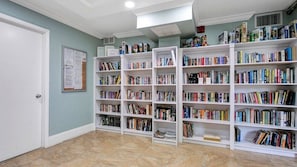 A library with white bookshelves filled with books, a bulletin board on the wall, and a door on the left.