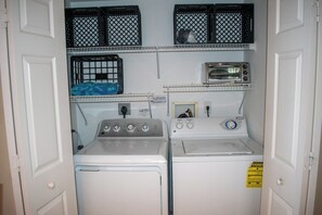 Une buanderie équipée de deux machines à laver, d’un sèche-linge et d’une petite étagère avec des paniers.