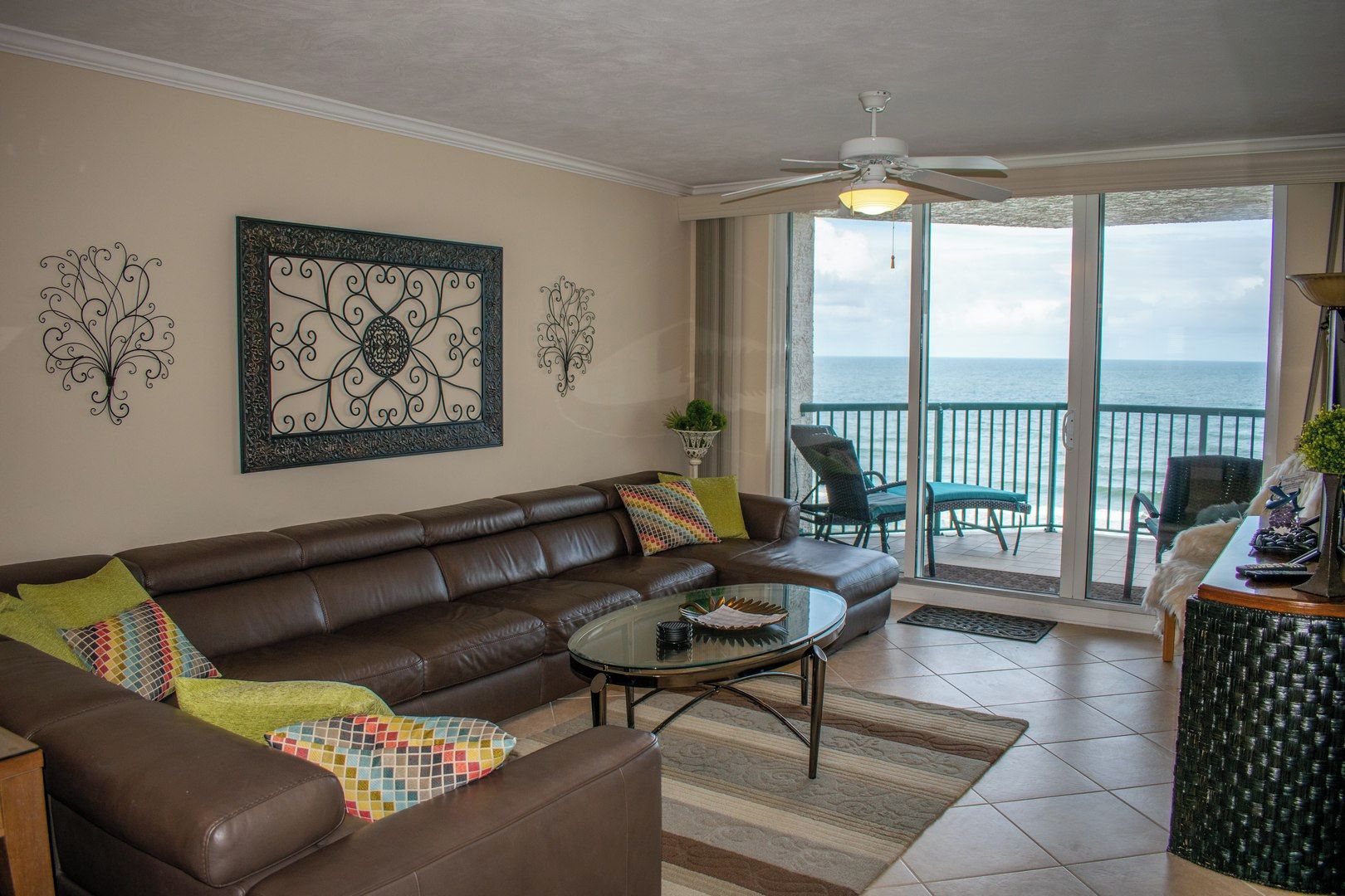 A living room with a brown leather sofa, a glass coffee table, and a view of the ocean through large sliding glass doors.