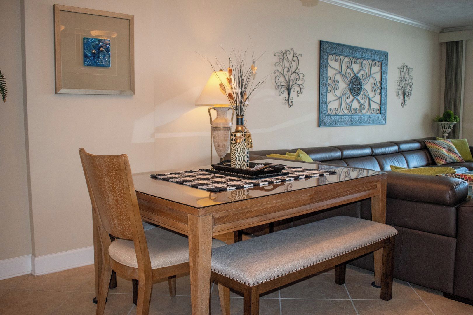Un comedor con una mesa de madera, sillas y un banco. Hay un florero con ramas sobre la mesa.