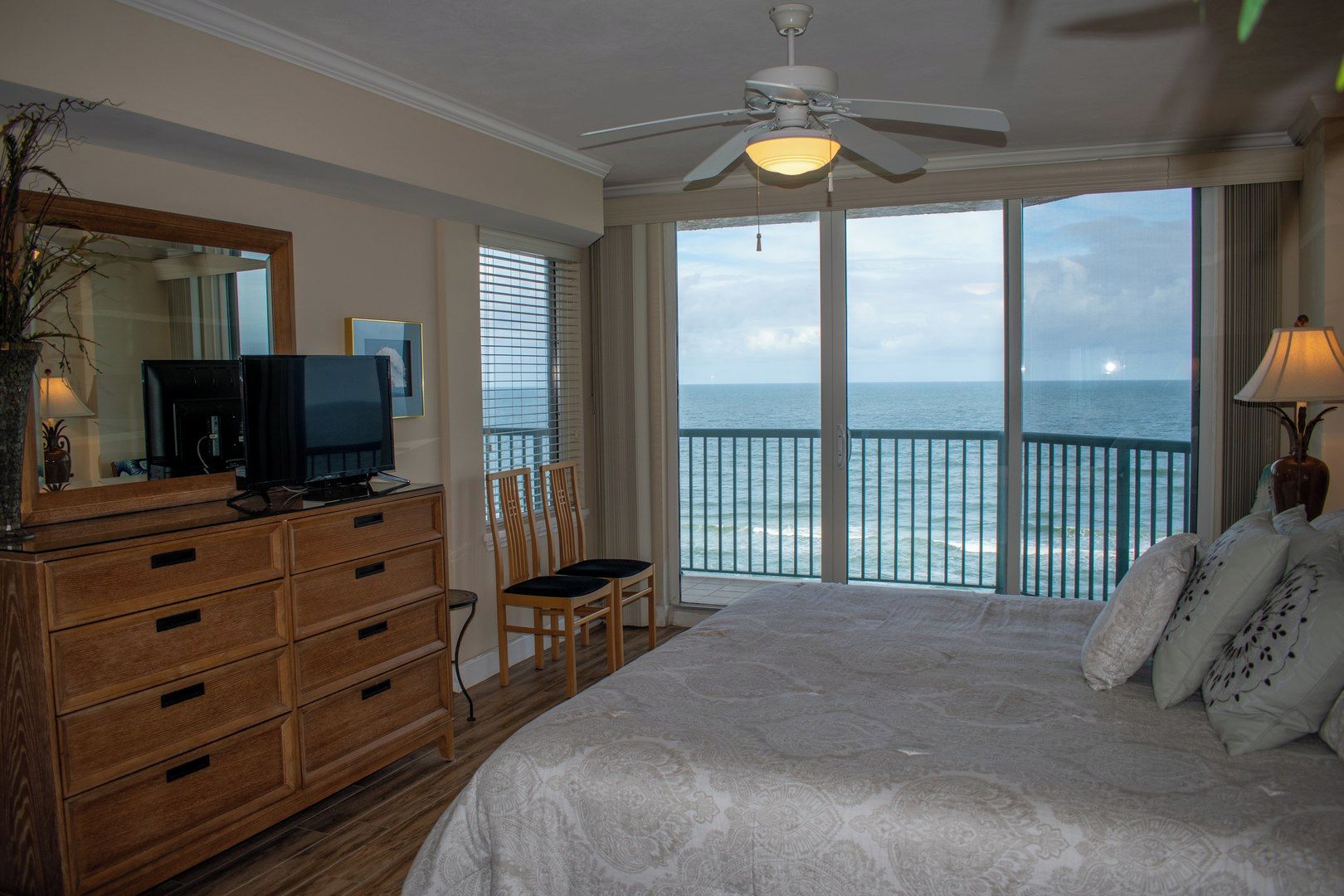 A bedroom with a large bed, a dresser, a television, and a view of the ocean through a balcony.